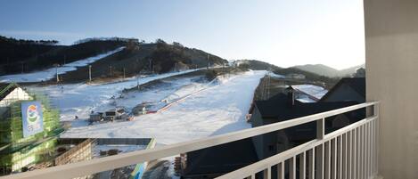 A balcony with a view of a snowy landscape, including a ski slope and a building with a sign.