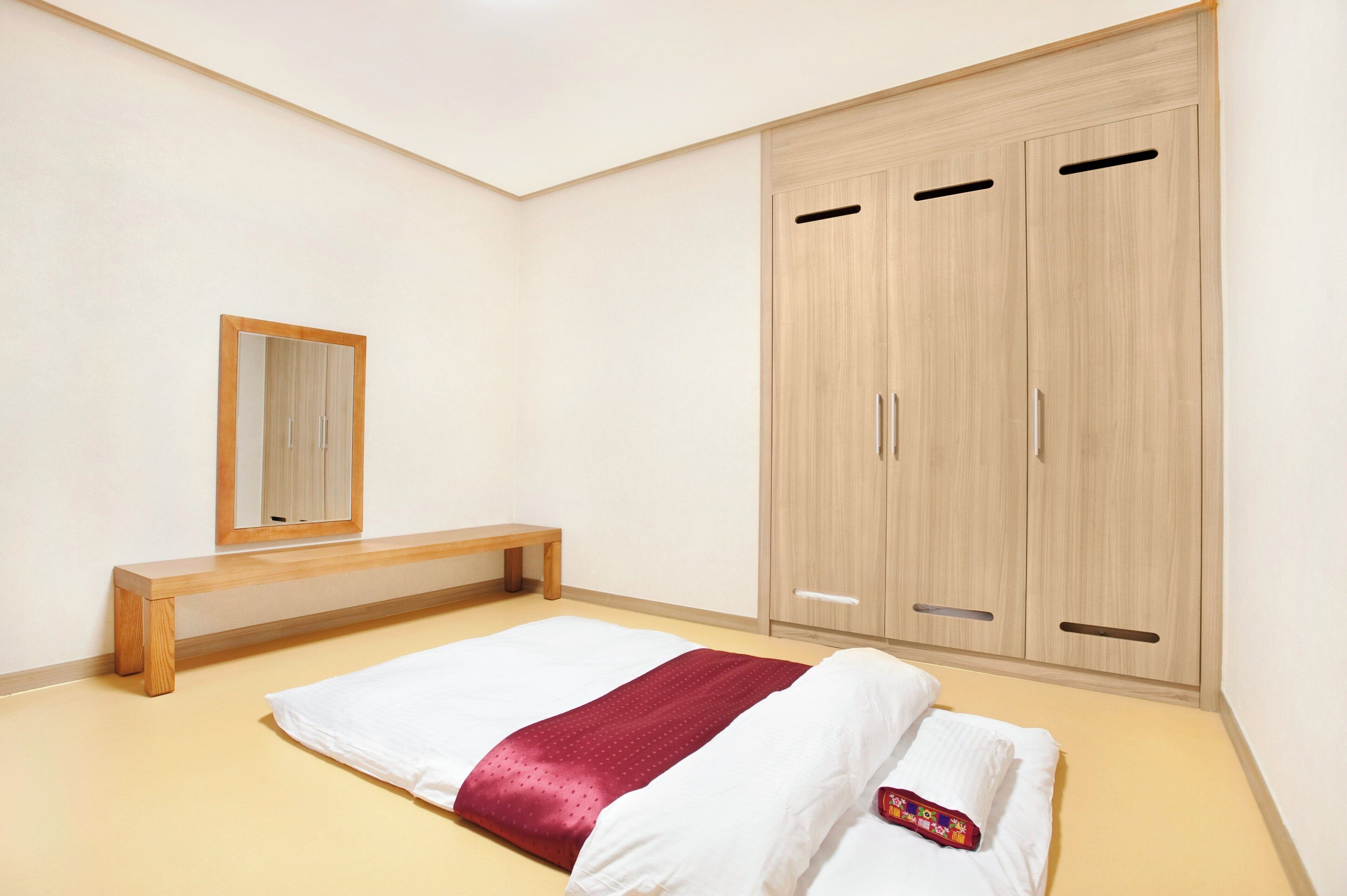 Un dormitorio con una cama, un banco de madera, un armario y un espejo.