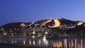 A large, illuminated hotel with multiple towers and a reflection in the water. - Holiday Inn Alpensia Pyeongchang Suites by IHG (Pyeongchang)