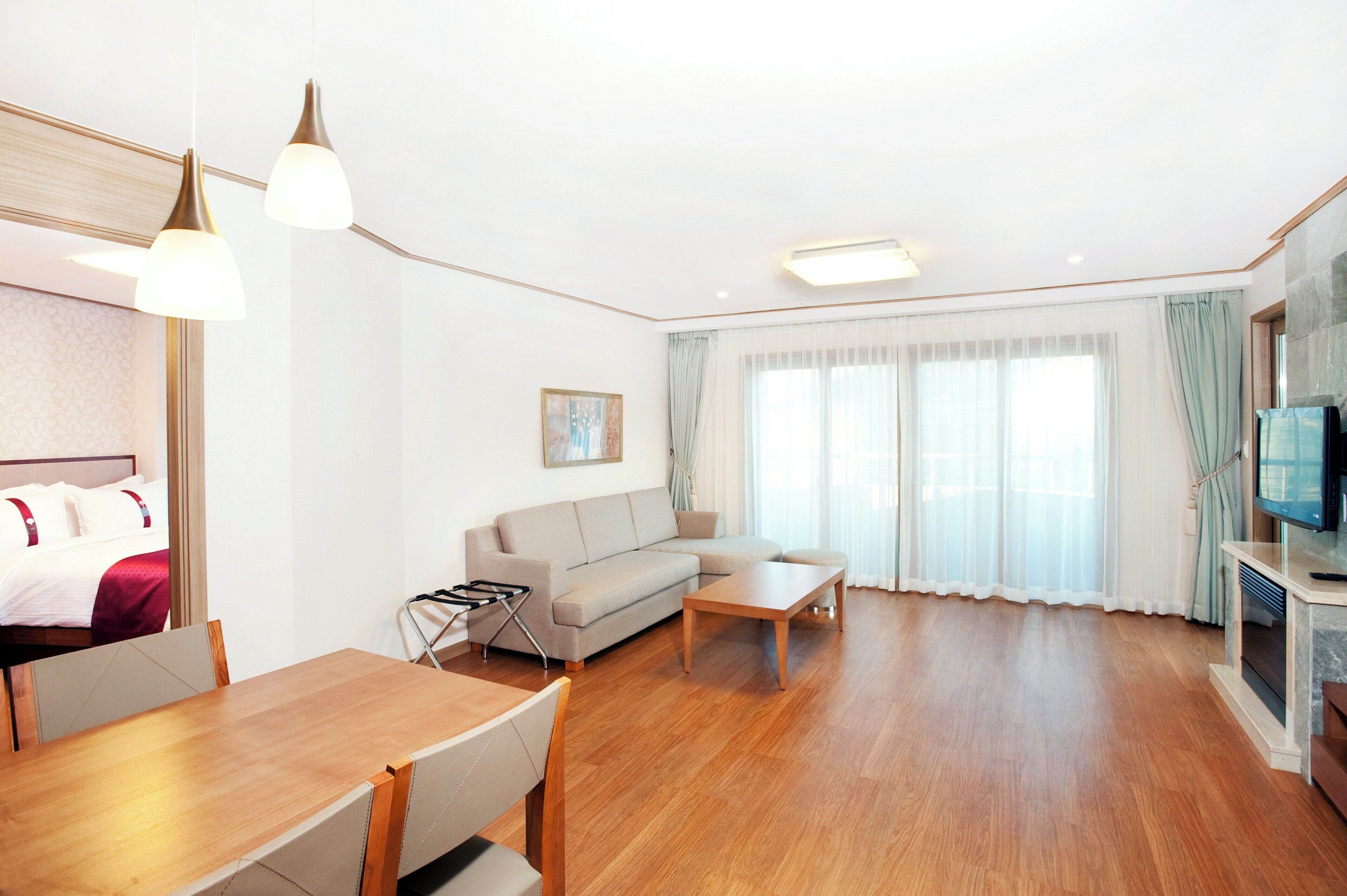 Una habitación de hotel moderna con piso de madera, un sofá, una mesa de comedor y un televisor.
