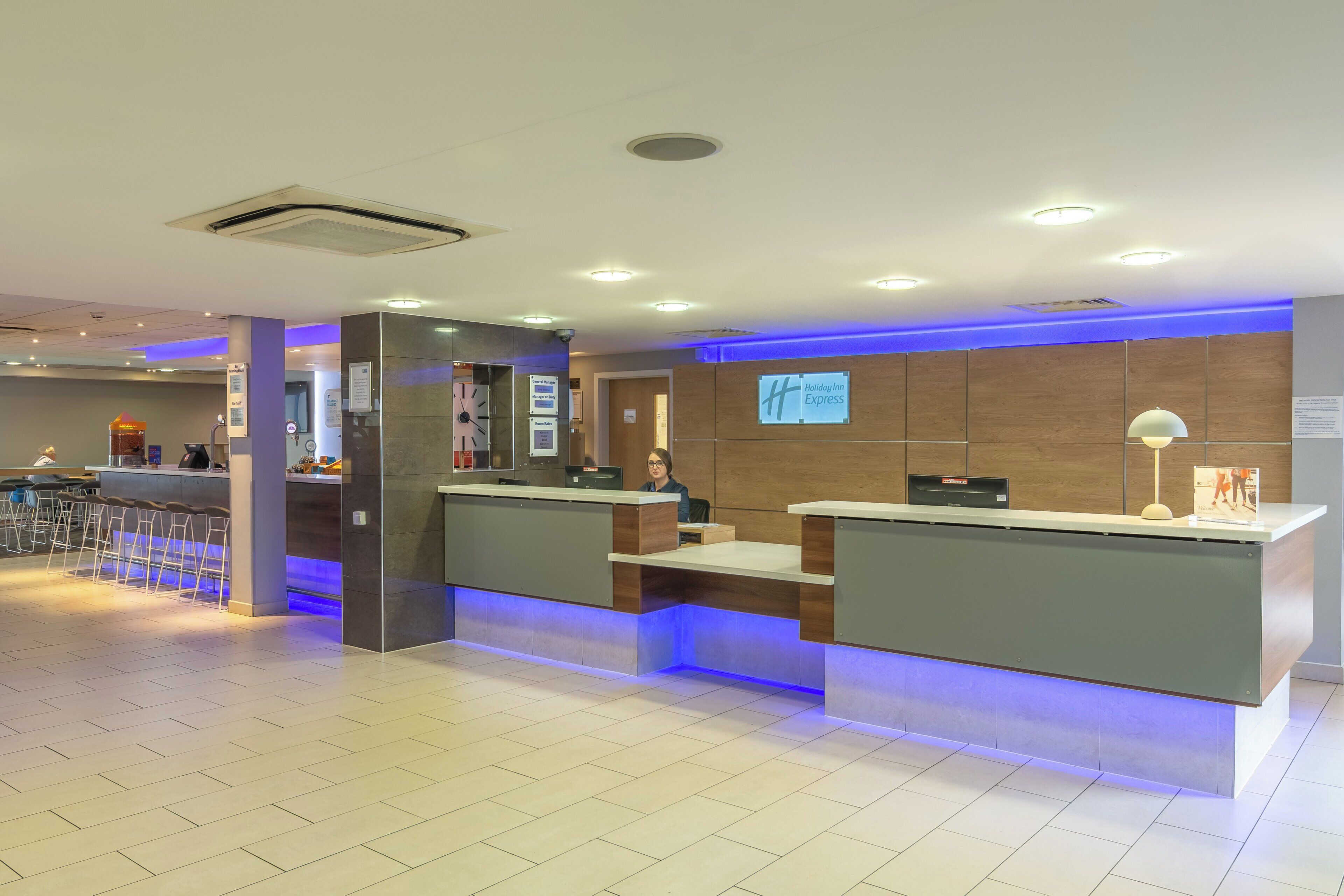Zona de recepción de un hotel con diseño moderno, que incluye un mostrador de recepción, un reloj digital y un letrero que indica Holiday Inn Express.