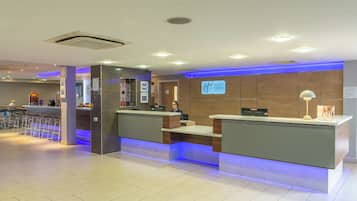 Zona de recepción de un hotel con diseño moderno, que incluye un mostrador de recepción, un reloj digital y un letrero que indica Holiday Inn Express.