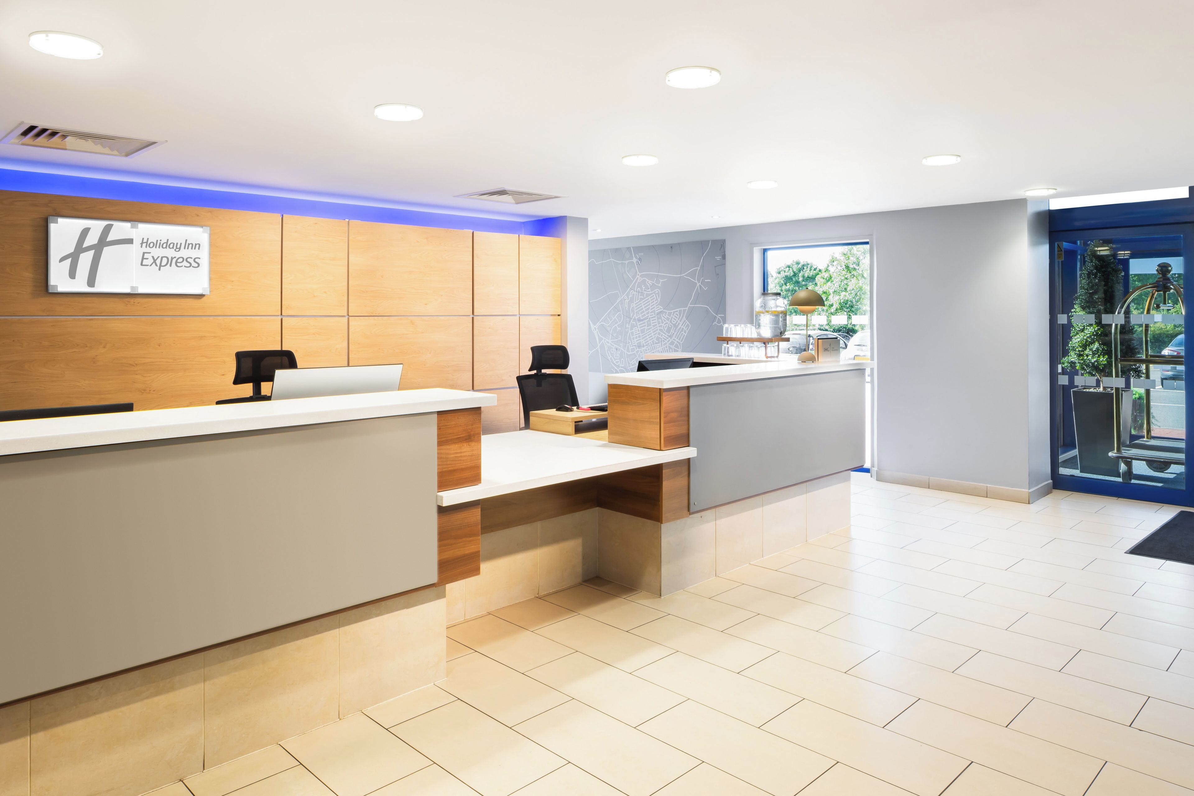 A hotel reception area with a wooden reception desk, a map on the wall, and a window with a view of the outdoors.