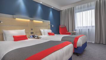 Een hotelkamer met twee bedden, een rode stoel, een tafeltje en een raam met gordijnen.