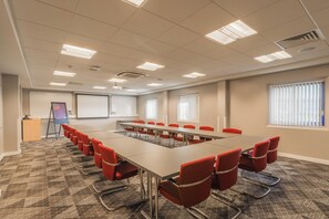 A conference room with a long table and red chairs, a projector screen, and a whiteboard.