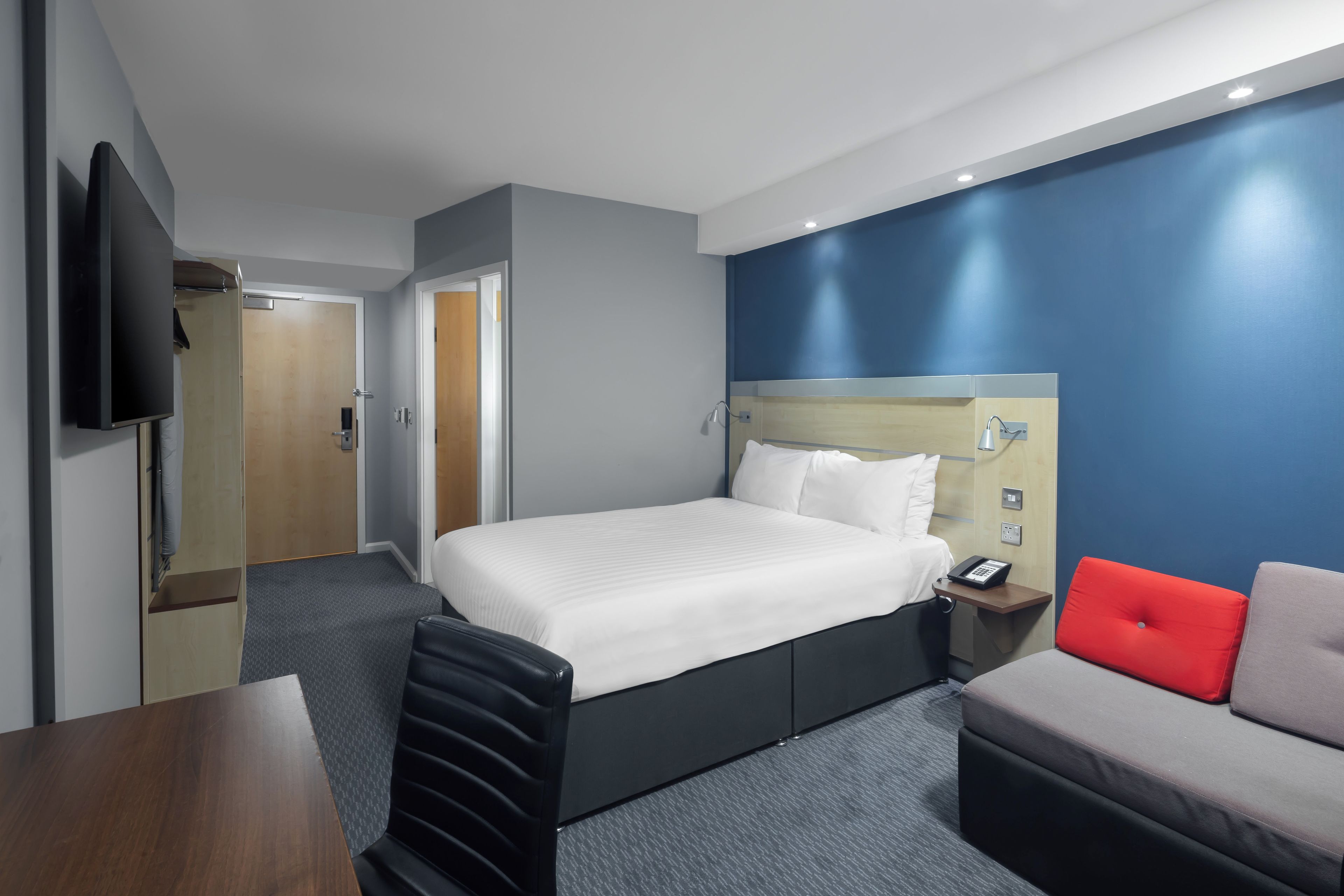 A hotel room with a bed, a desk, a chair, a sofa, and a television.
