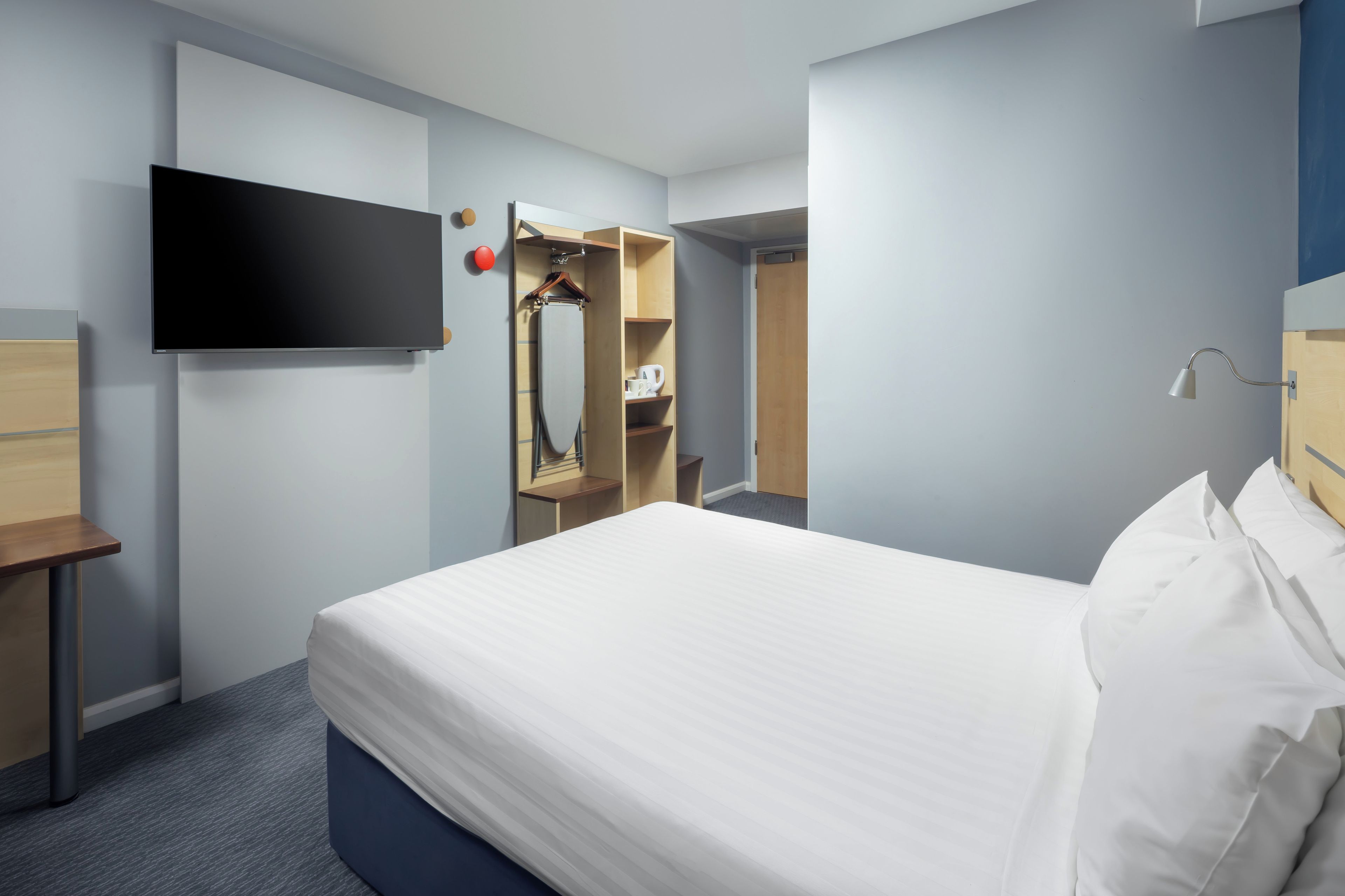Ein Hotelzimmer mit einem Bett, einem an der Wand befestigten Flachbildfernseher, einem Holzschrank und einem Spiegel.