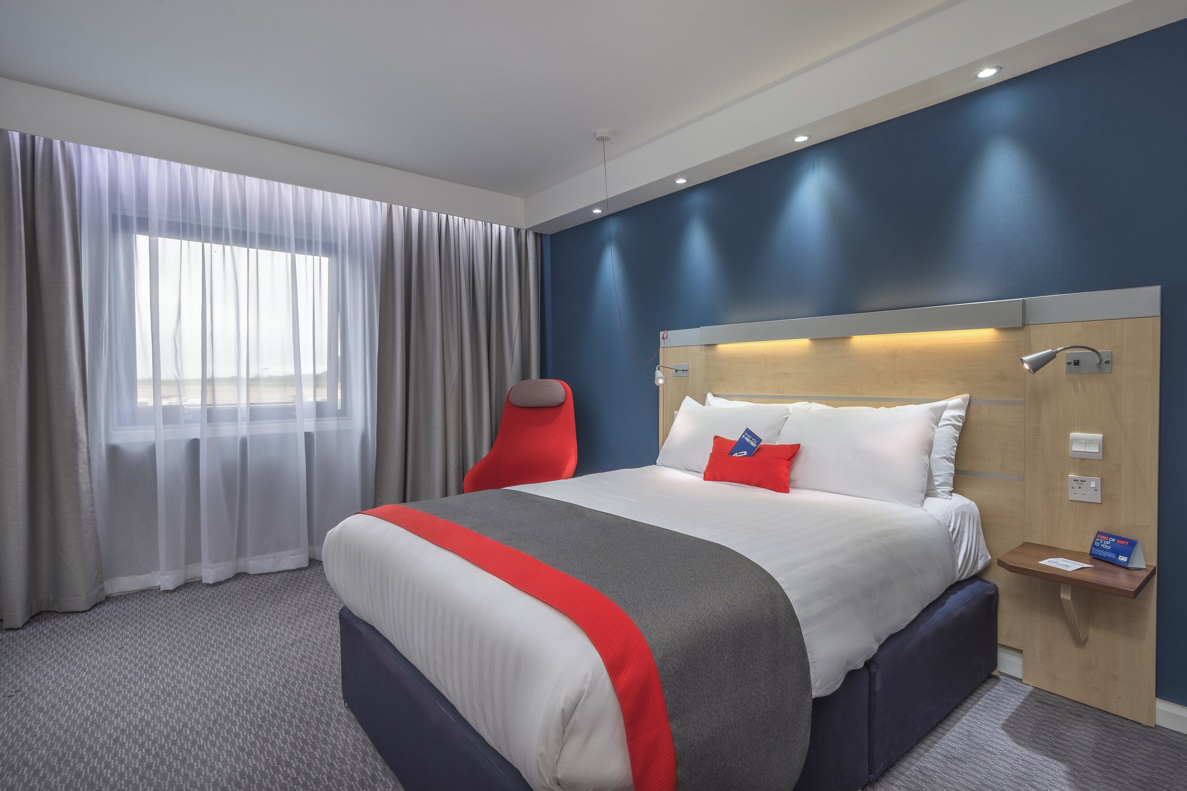 A hotel room with a large bed, a bedside table, a chair, and a window with curtains.