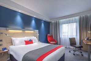 A hotel room with a bed, a desk, a chair, and a window with curtains.