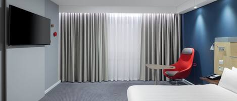 A hotel room with a bed, a red chair, a TV, and a large window with curtains.