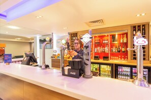 A bar area with a counter, a person pouring a drink, and shelves with bottles.
