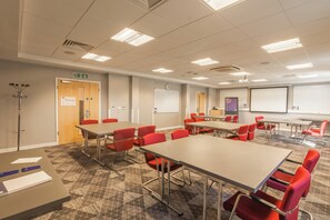 A conference room with multiple tables and chairs, a whiteboard, and a projector screen.
