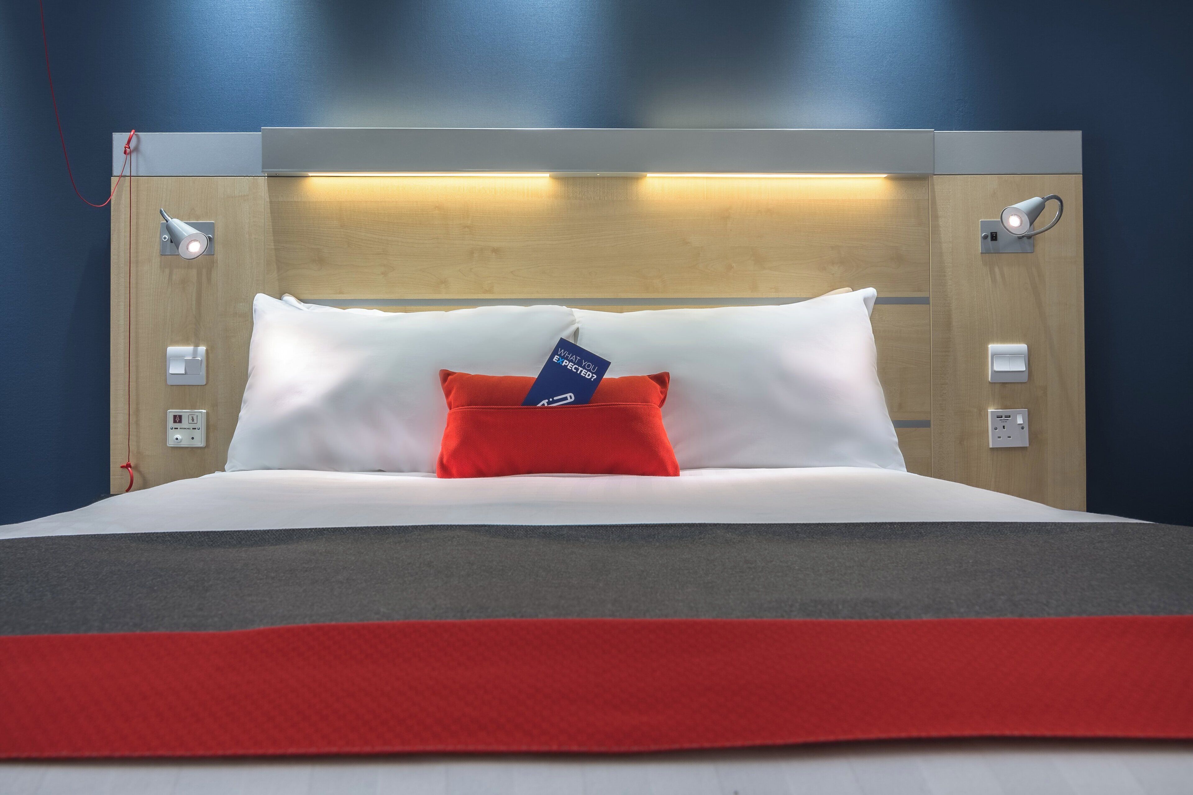 A hotel room with a bed, a red pillow, a blue tag, and a wooden headboard.