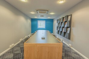 A conference room with a long table, chairs, a window with blinds, and a wall with magazine holders.