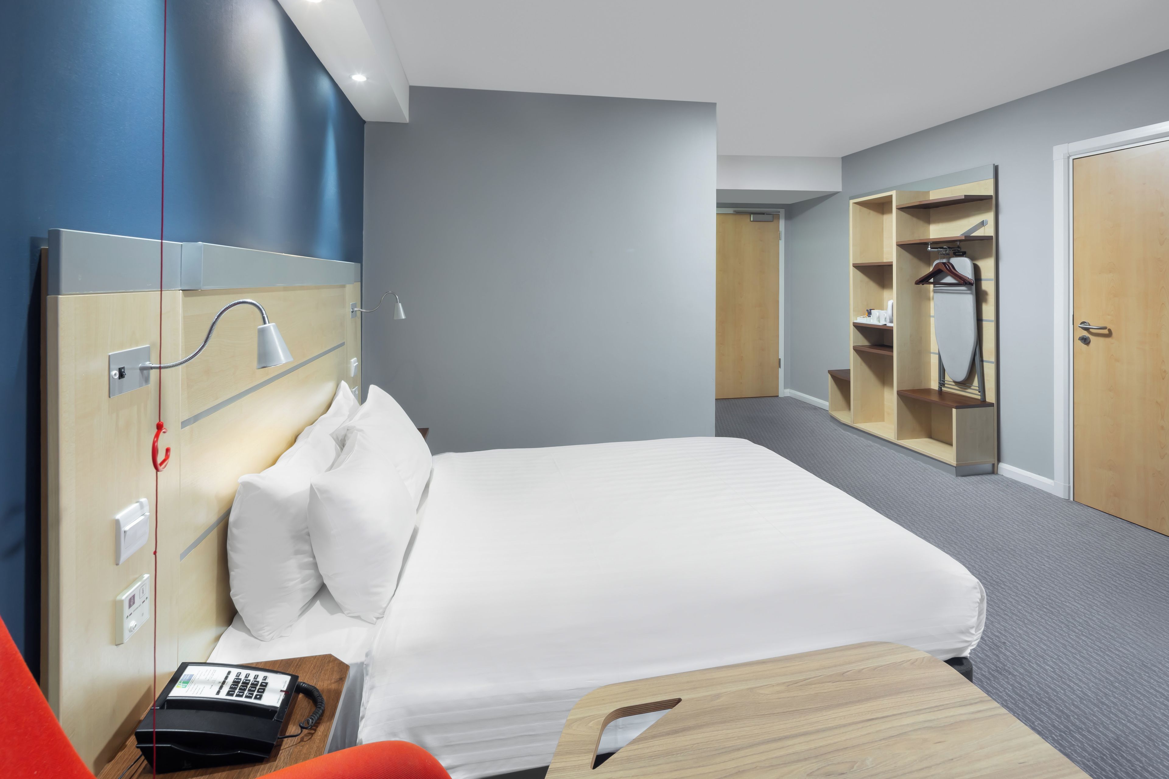 A hotel room with a bed, a desk with a telephone, a mirror, and a wardrobe.