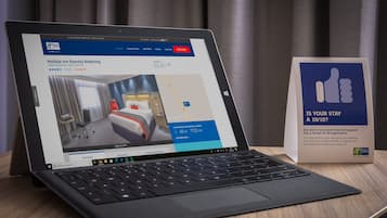 A laptop displaying a hotel booking page for Holiday Inn Express Kettering, with a 4.5-star rating and a price of 62.40 GBP per night.