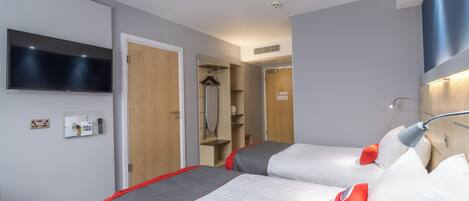 A hotel room with two beds, a TV, a mirror, a coat rack, and a shower area.