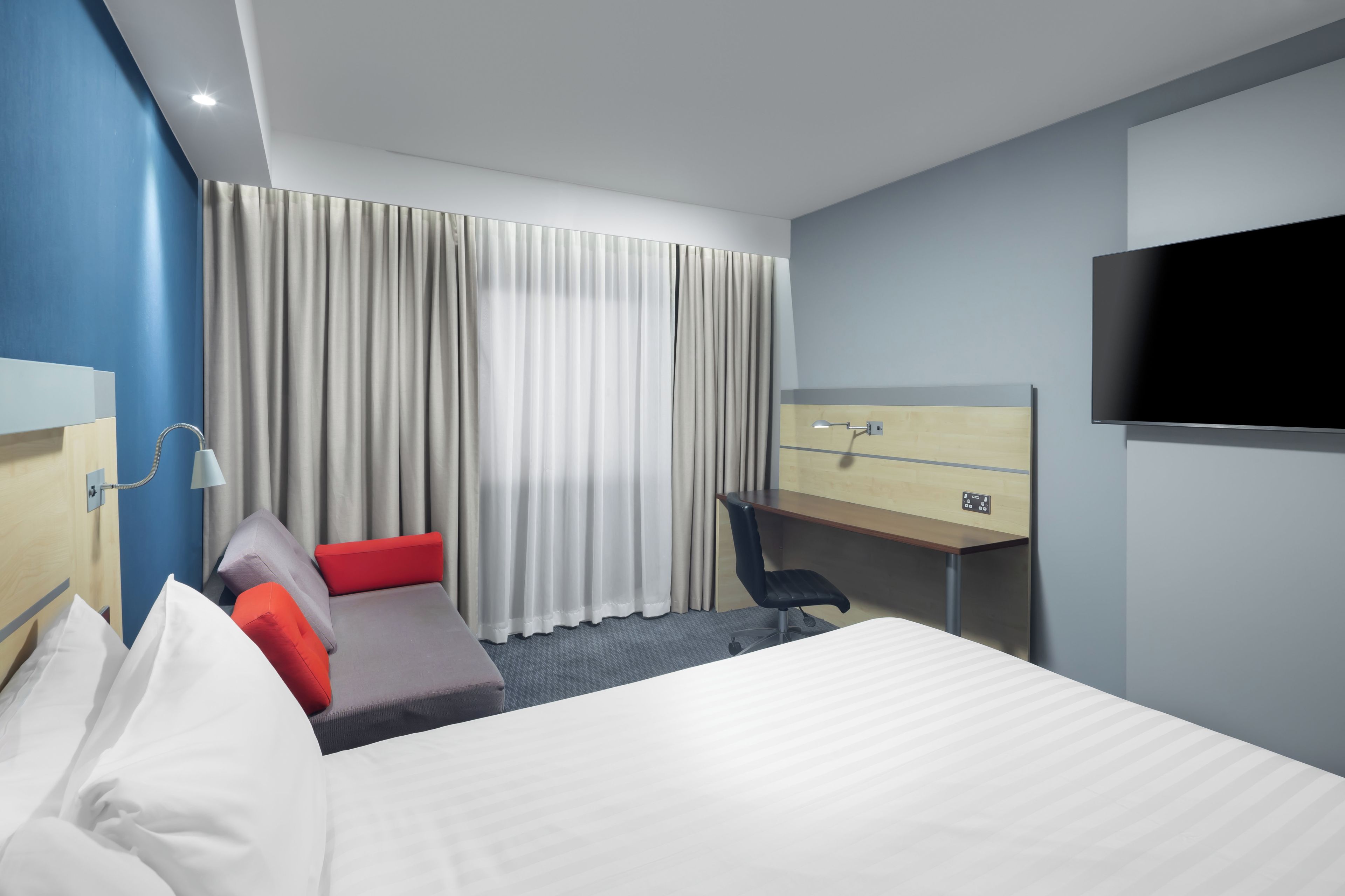 A hotel room with a bed, a desk, a chair, a TV, and curtains.