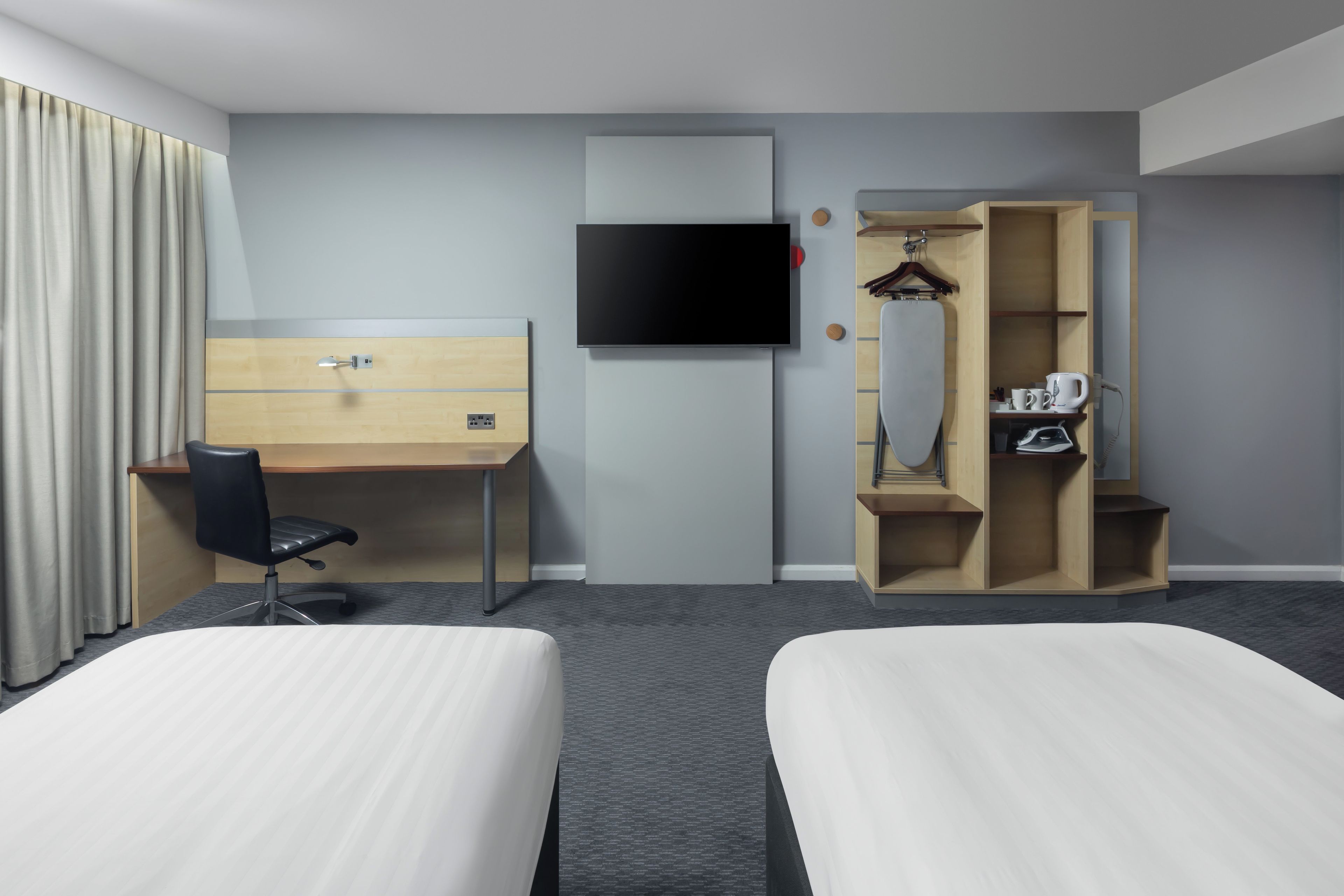 A hotel room with two beds, a desk, a chair, a TV, a wardrobe, and a mirror.