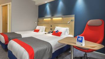 A hotel room with two beds, a red chair, a wooden table, and a sign on the table.