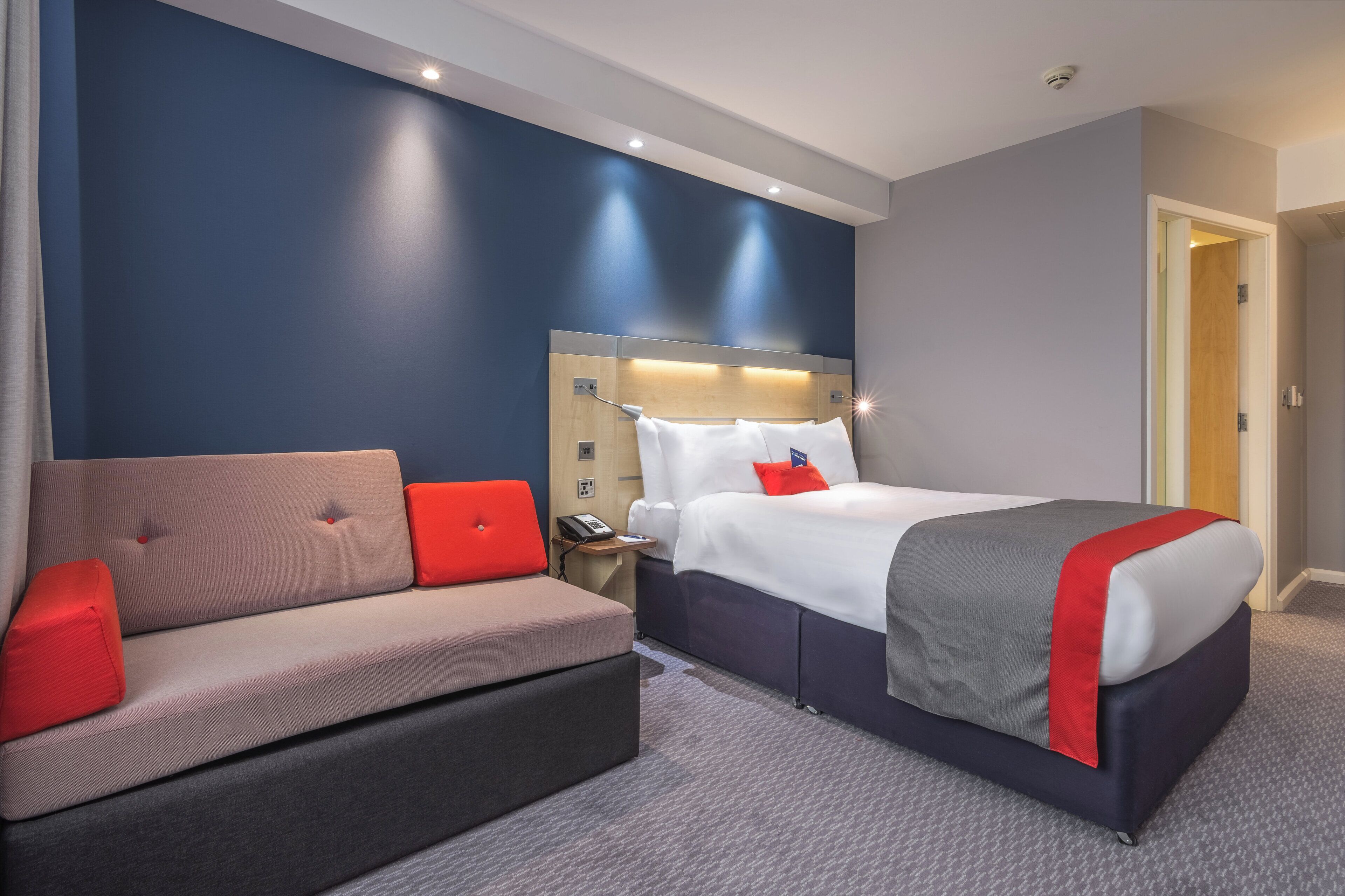 A hotel room with a bed, a sofa, a bedside table, and a nightstand.