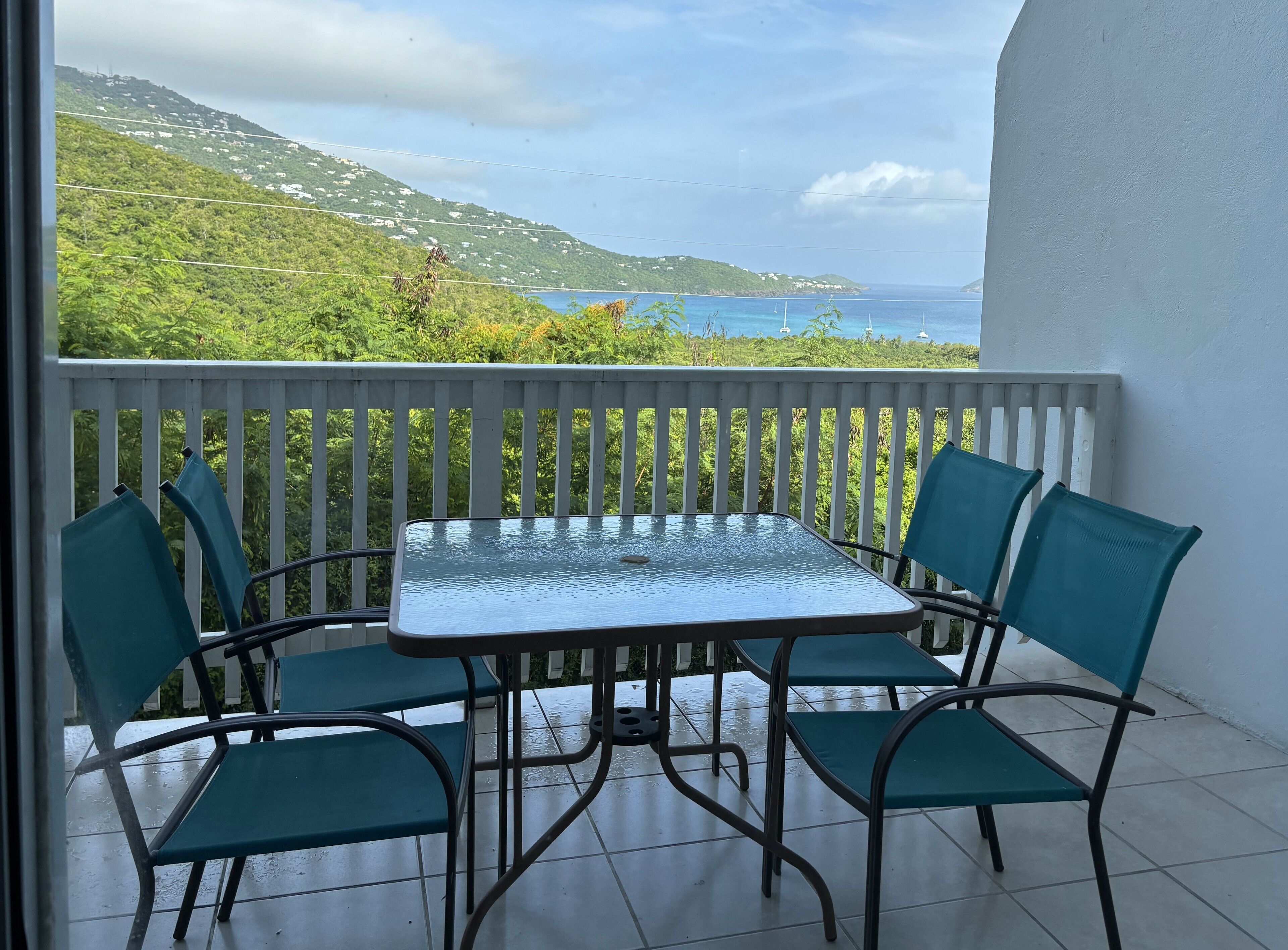 A balcony with a table and chairs, overlooking a coastal landscape with houses and greenery.