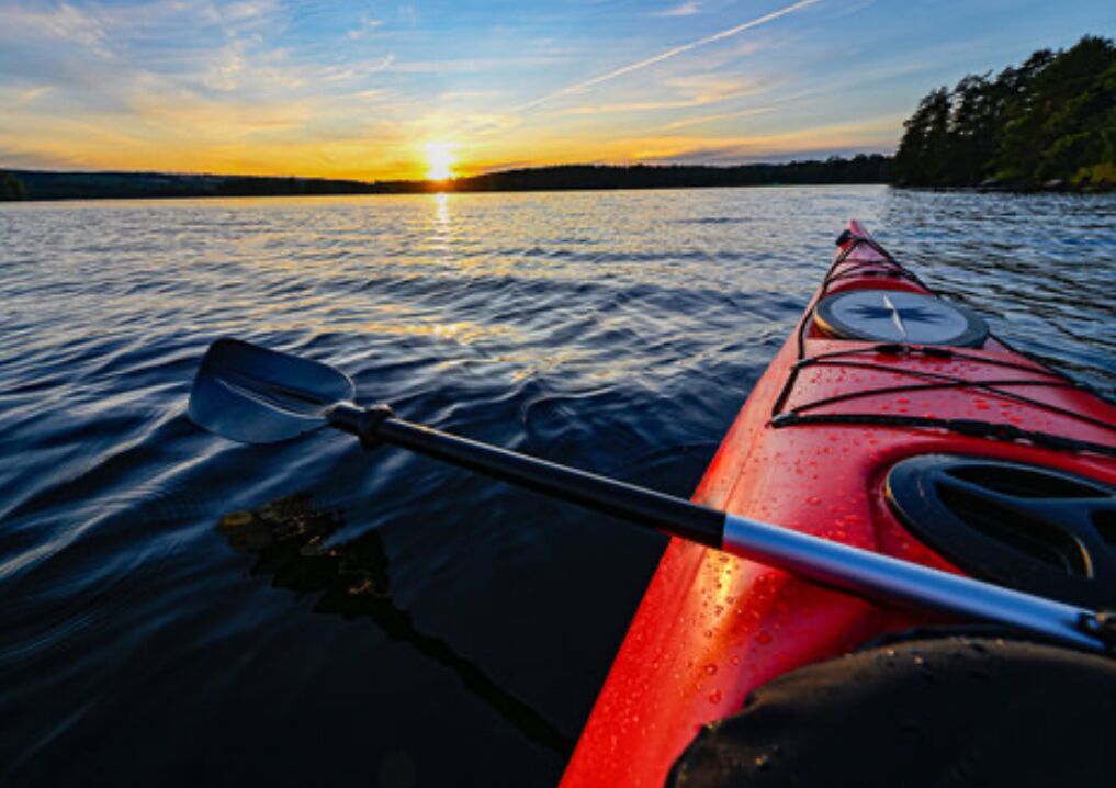 Ein Kajak auf ruhigem Wasser, im Hintergrund ein Sonnenuntergang.