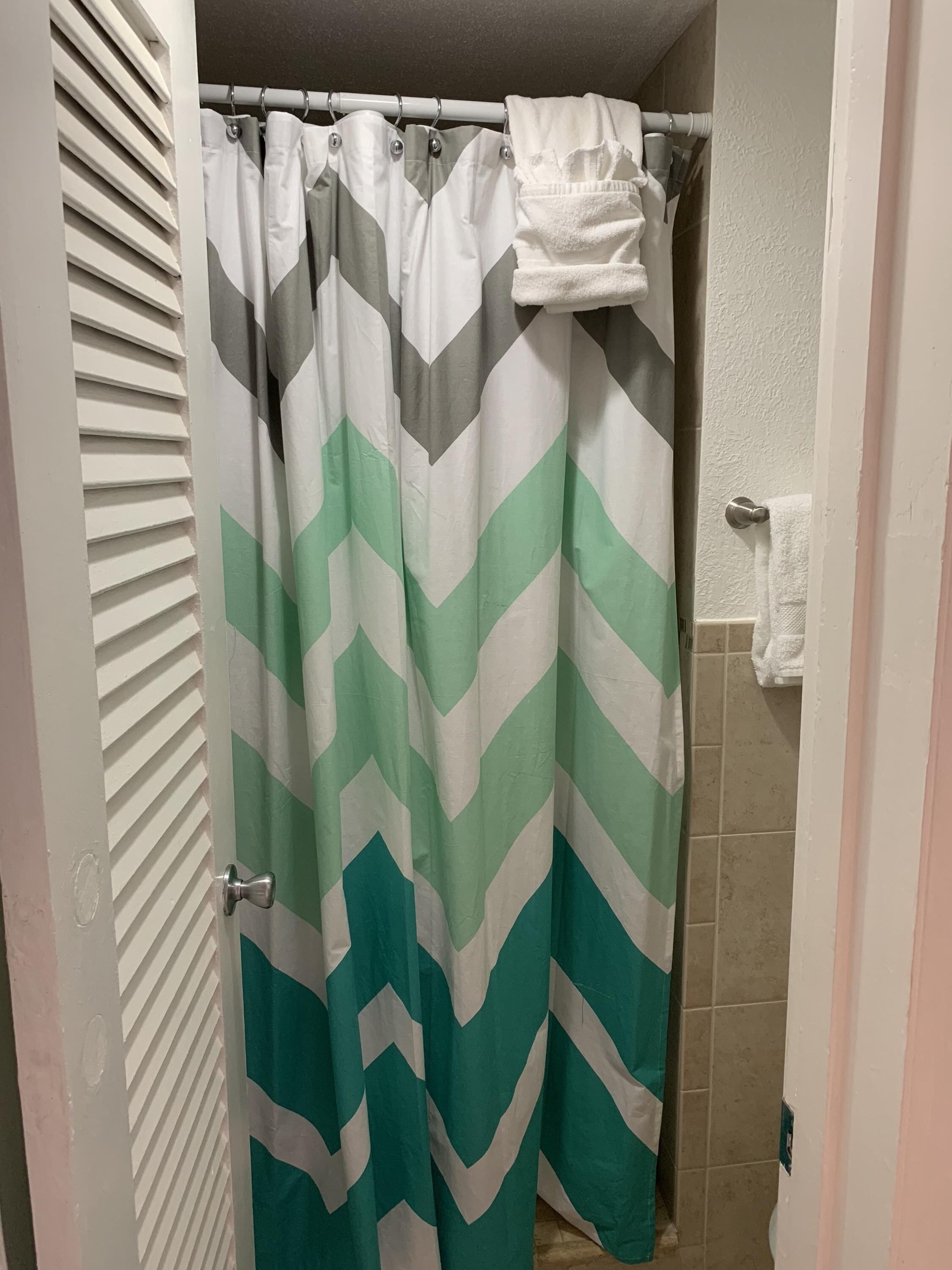 A bathroom with a shower curtain featuring a chevron pattern in shades of green and white.