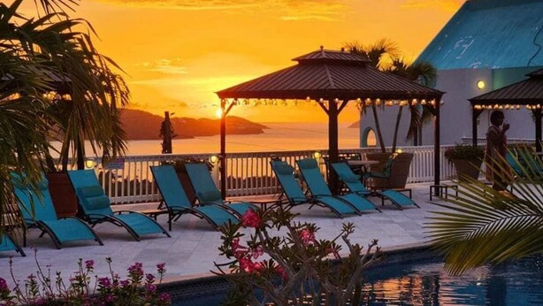 Un espace aménagé au bord de la piscine, avec des chaises longues et des parasols, offrant une vue sur une étendue d’eau au coucher du soleil.