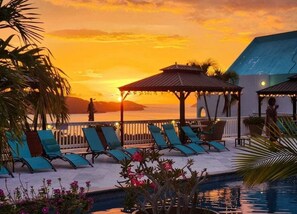 A poolside area with lounge chairs and umbrellas, overlooking a body of water during sunset. - Flamboyan on the Bay Resort and Villas (St. Thomas)