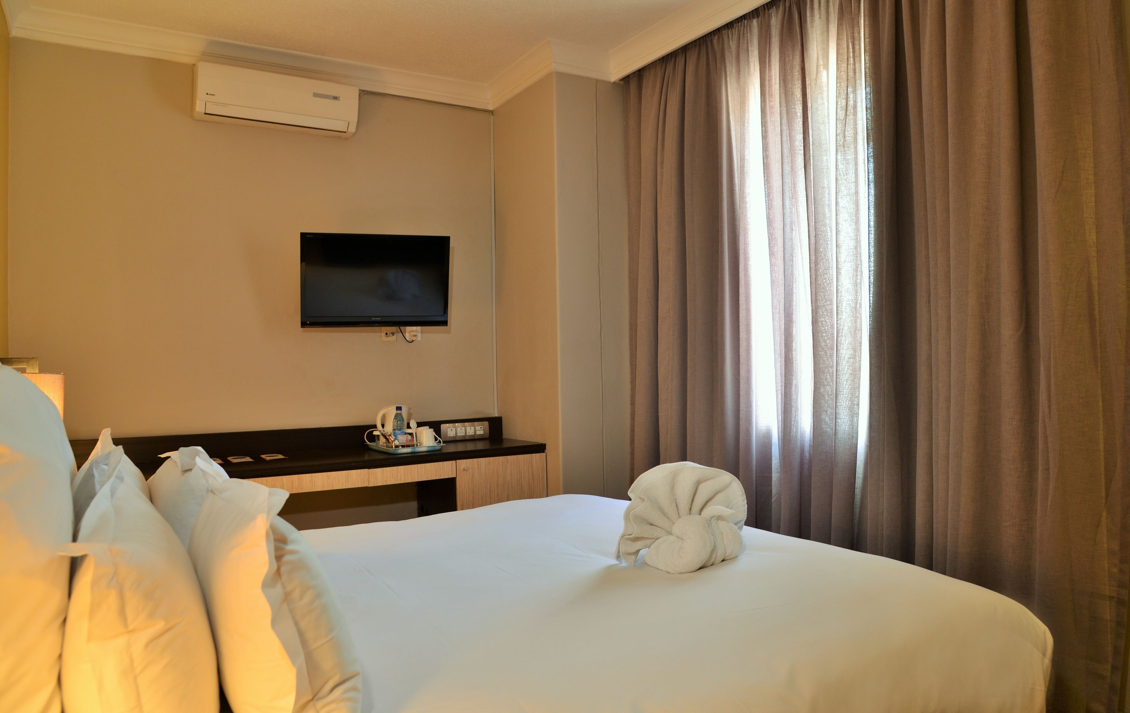 Habitación de hotel con cama, televisión de pantalla plana en la pared, mesita de noche con bandeja y ventana con cortinas.