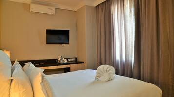 A hotel room with a bed, a flat-screen TV mounted on the wall, a bedside table with a tray, and a window with curtains.