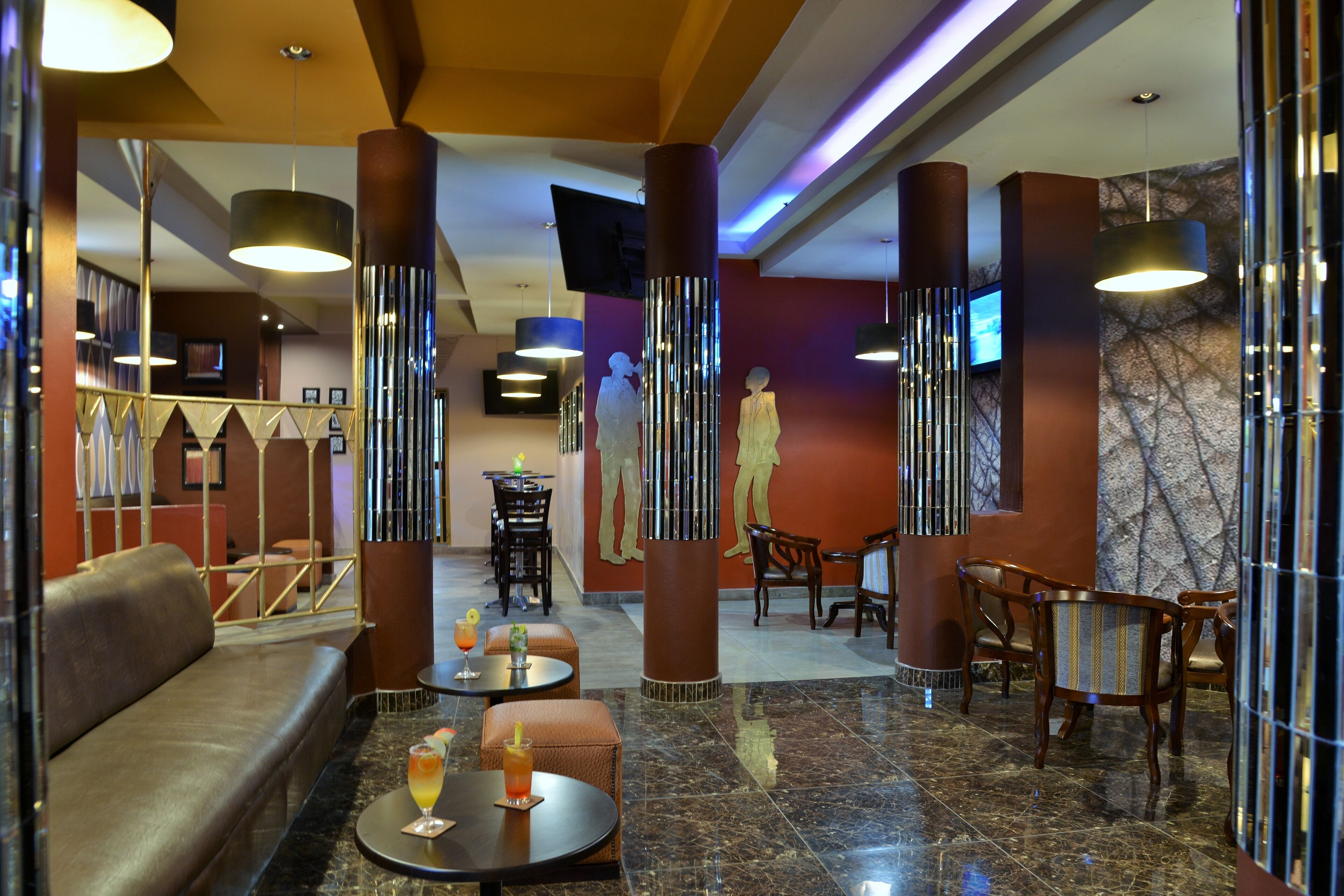 A lobby with a sofa, round tables, and chairs, a TV mounted on the wall, and a marble floor.