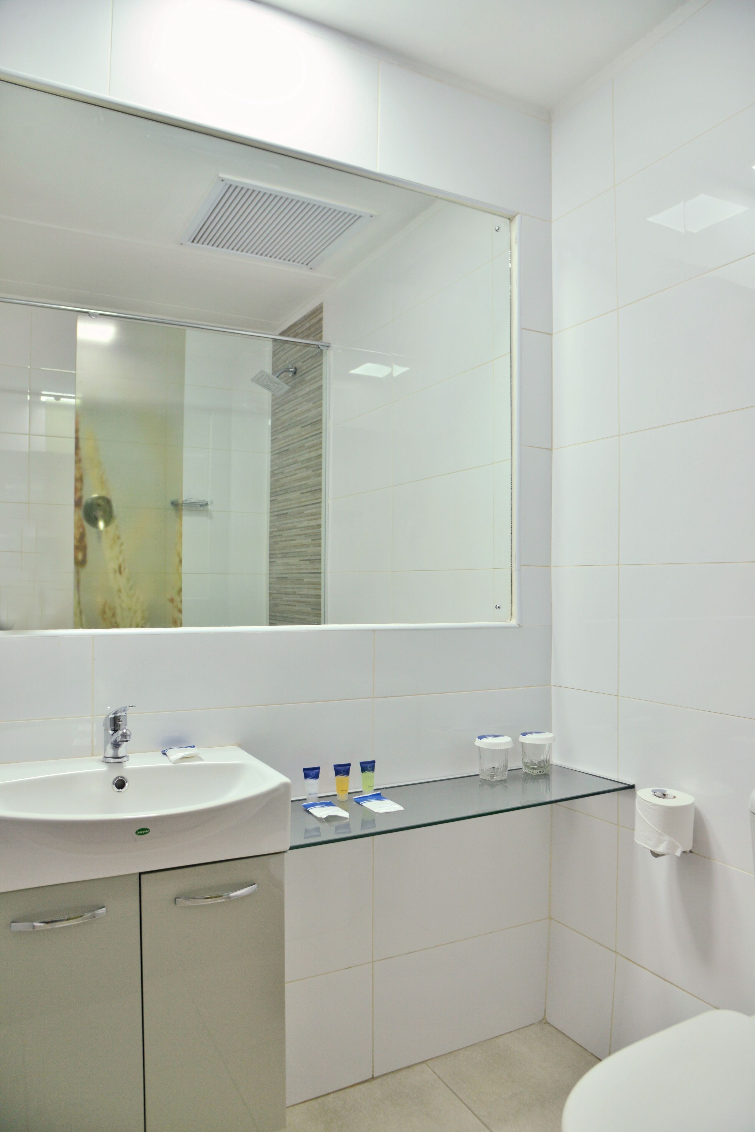 A modern bathroom with a glass sink, a large mirror, and a toilet.