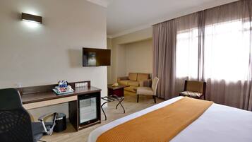 A hotel room with a bed, desk, chair, TV, and a view of the outside through a window.