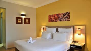 Habitación de hotel con una cama grande, dos lámparas fijadas a la pared, una mesita de noche con un teléfono y dos cuadros enmarcados.