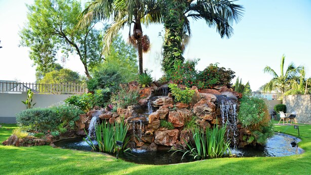 A landscaped garden with a pond, waterfalls, and tropical plants.