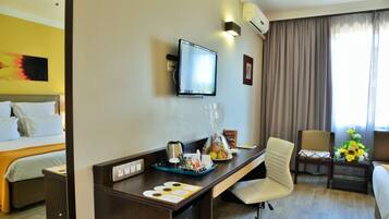 Habitación de hotel con cama, escritorio, silla y televisor en la pared.