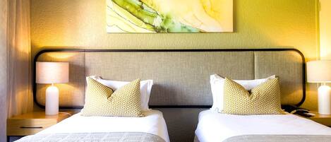 Quarto de hotel com duas camas, uma grande pintura abstrata na parede e uma cabeceira moderna.