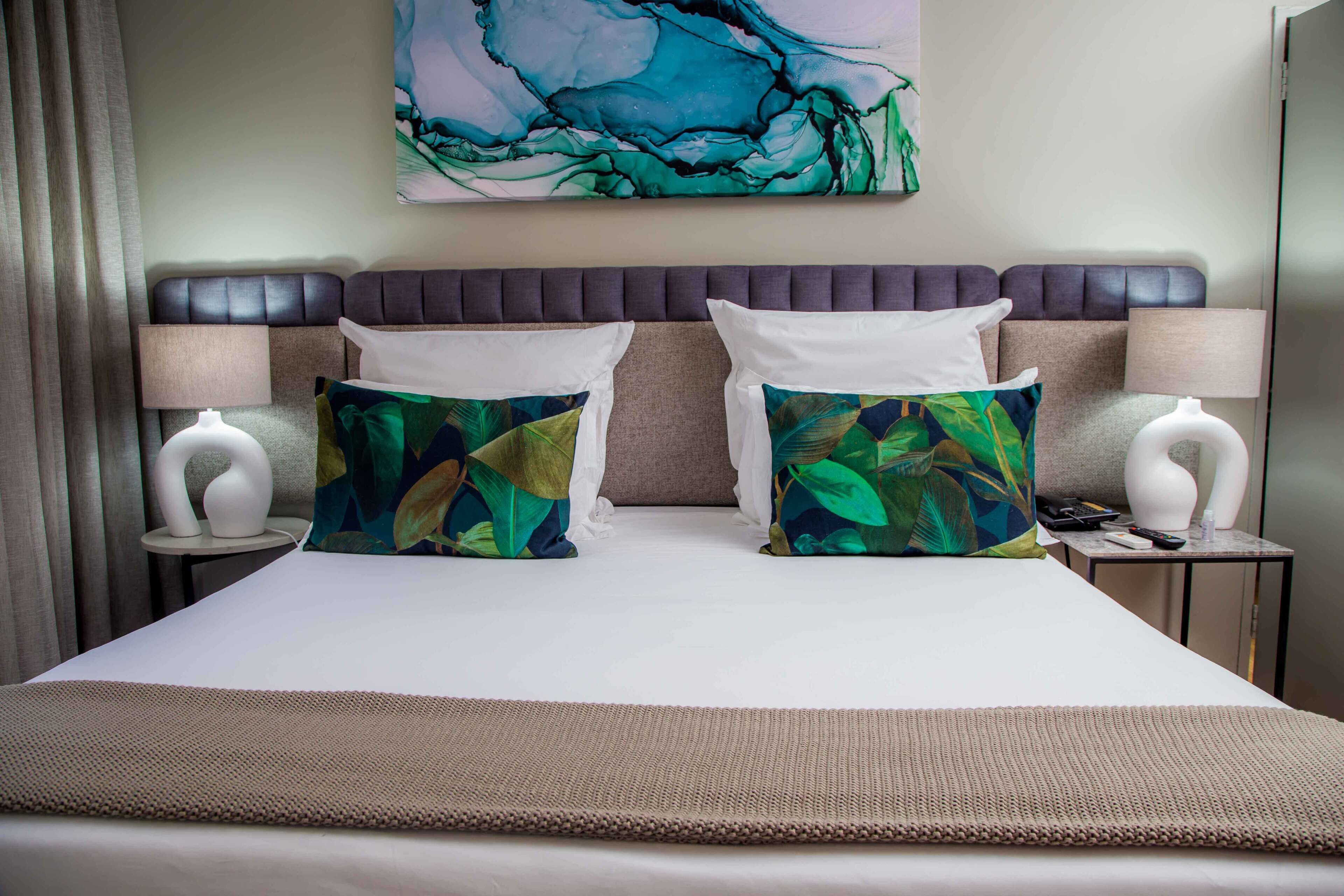 A hotel room with a large bed, two nightstands, a headboard, and a painting on the wall.