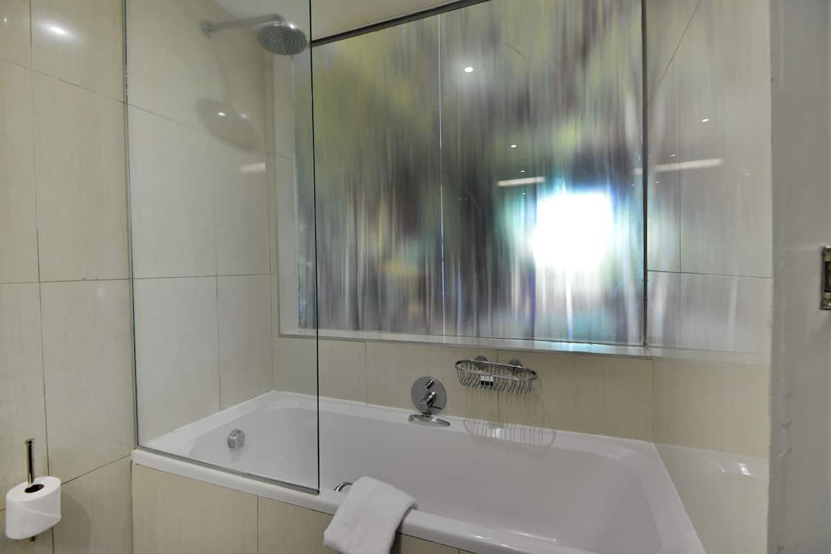 A modern bathroom with a glass-enclosed shower, a white bathtub, and a visible toilet paper holder.