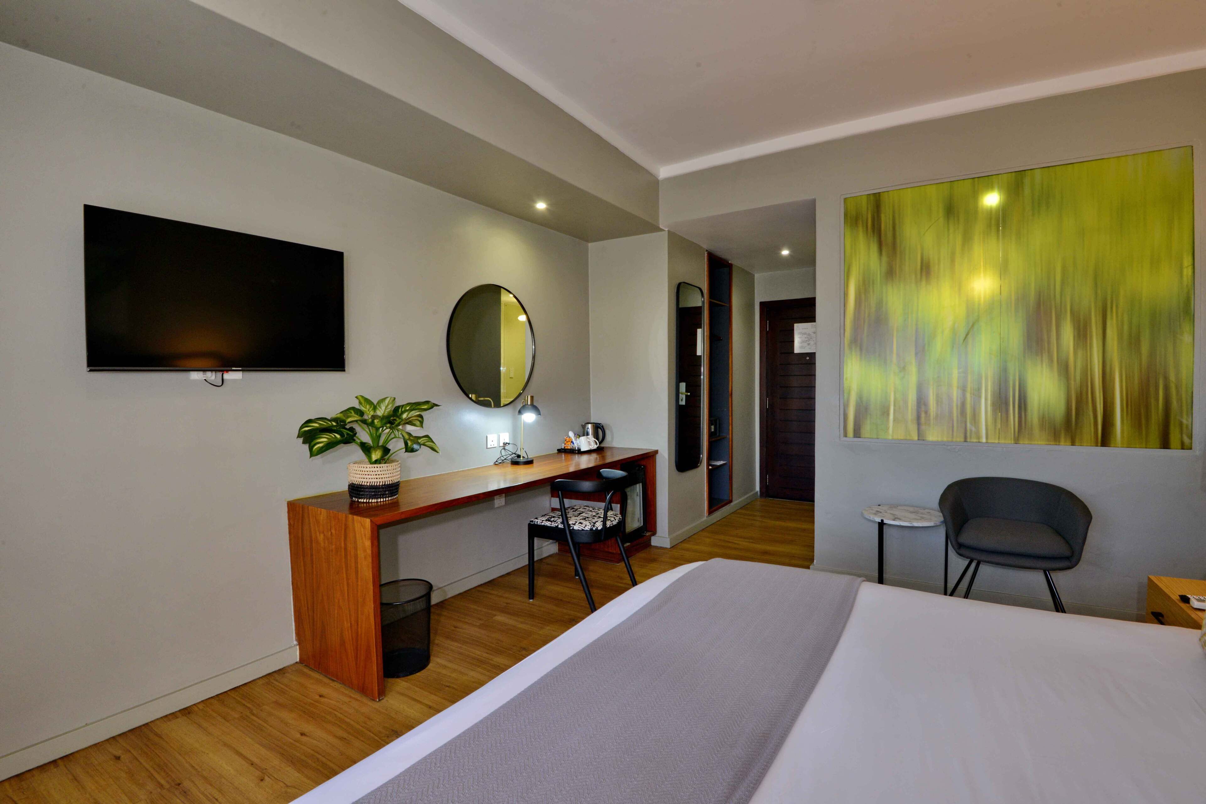 A modern hotel room with a large bed, a desk with a computer, a chair, a TV, a mirror, and a large abstract painting on the wall.