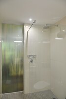 A glass-enclosed shower with a handheld showerhead and a wall-mounted faucet.