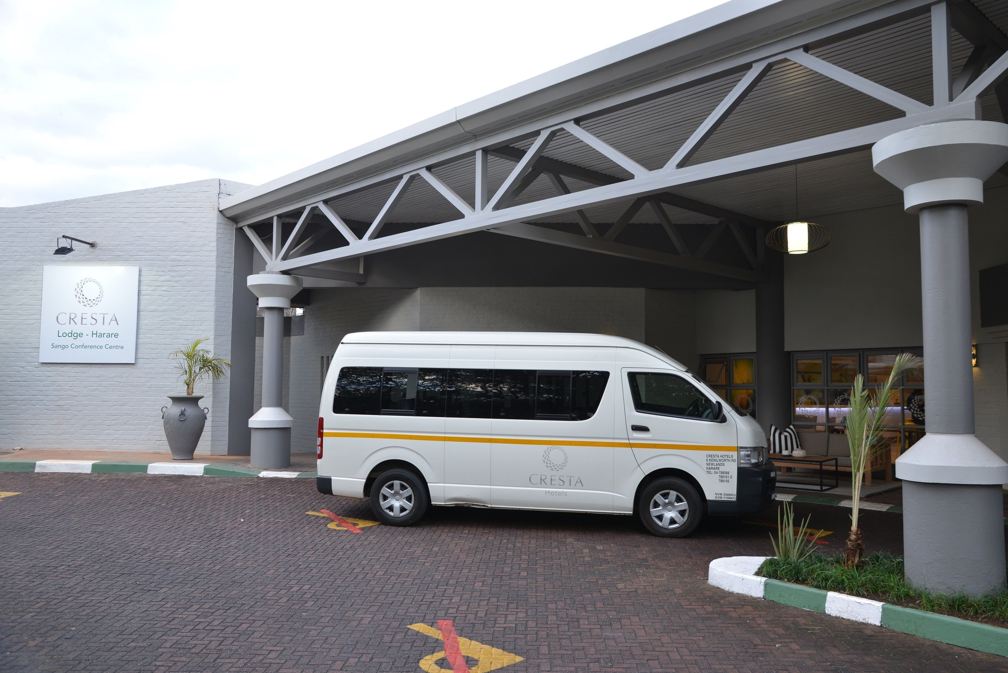 A white van parked in front of a building with a sign reading "CRESTA Lodge - Harare Sango Conference Centre."