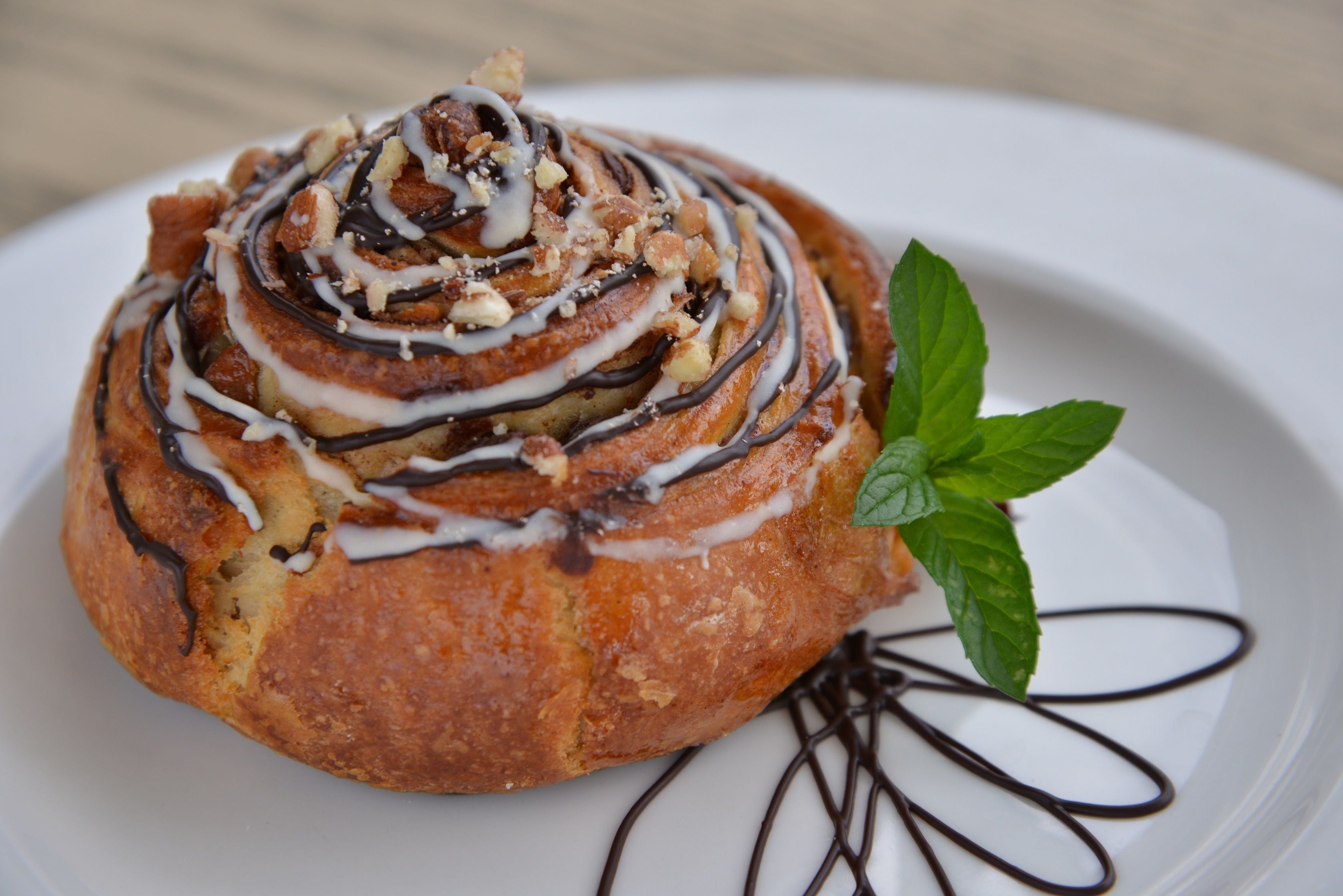 Un roll de canela con glaseado de chocolate y nueces sobre un plato blanco.