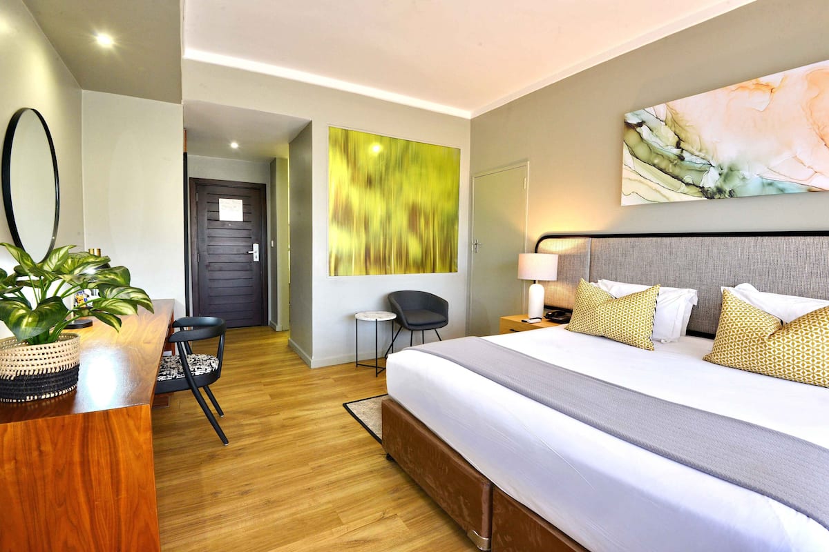 A modern hotel room with a large bed, a desk, a chair, and a small table.
