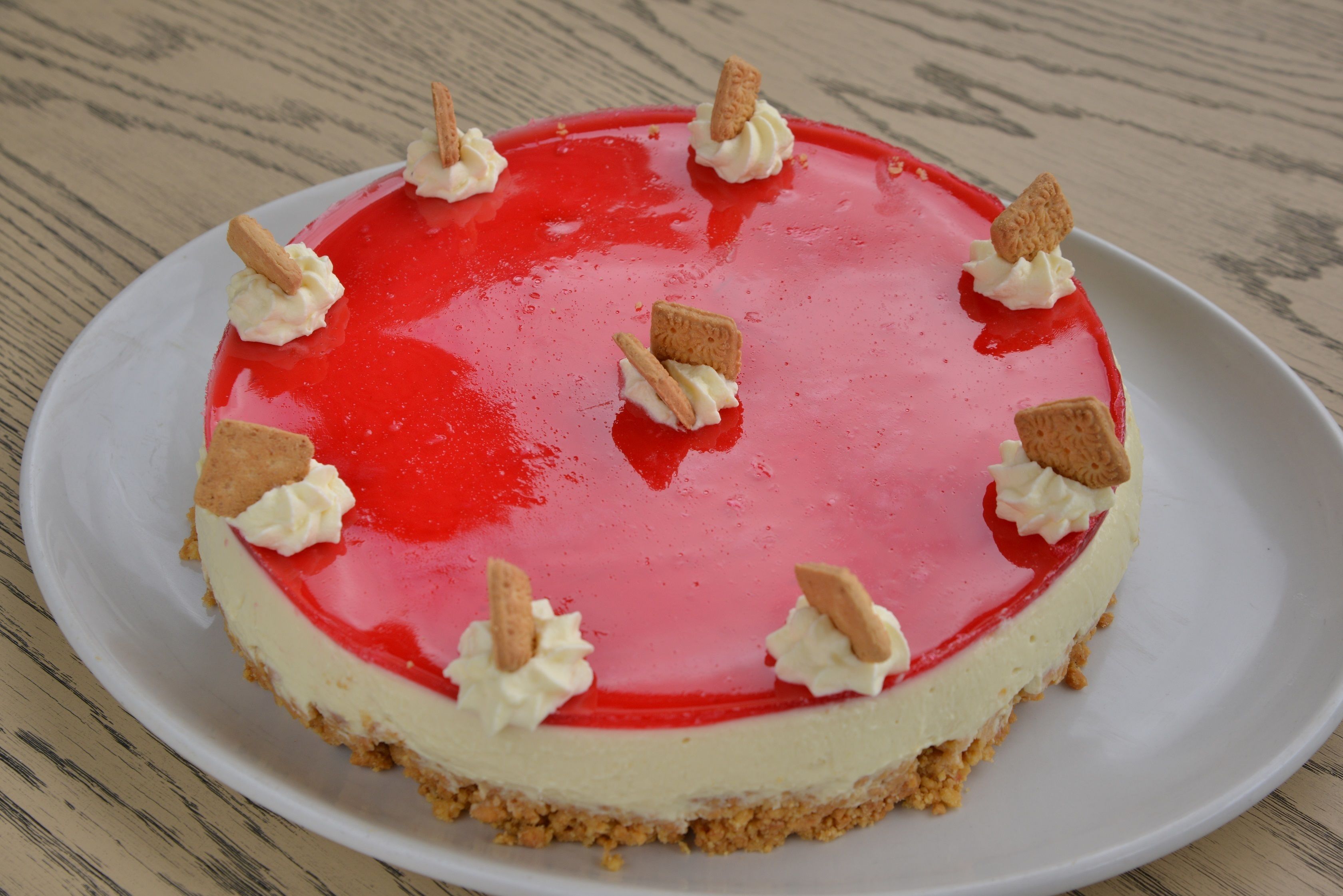 A cheesecake with a red glaze and cream on a white plate.