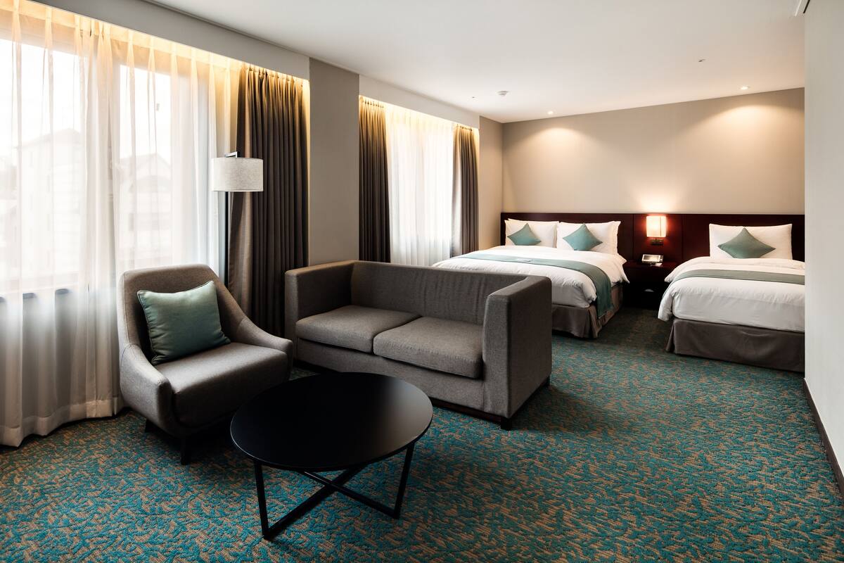 A hotel room with a sofa, a small table, two beds, and a lamp.