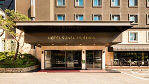A modern hotel entrance with a glass facade, a covered entrance area, and a landscaped garden. - Hotel Sunshine Seoul (Seoul)