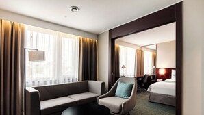 A hotel room with a sofa, armchair, and a small table. There is a bed in the background and a window with curtains. - Hotel Sunshine Seoul (Seoul)